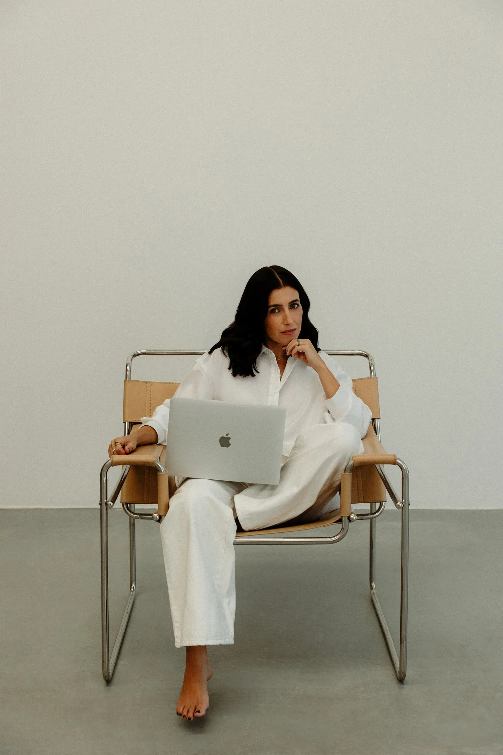 Liana McLeod sitting in a leather and chrome armchair with a laptop on her lap.